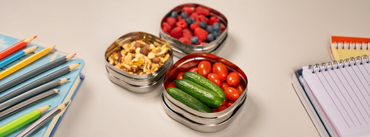 Stainless steel fruit bowls and snack boxes with fruit, pencil, notebooks, books on a school table