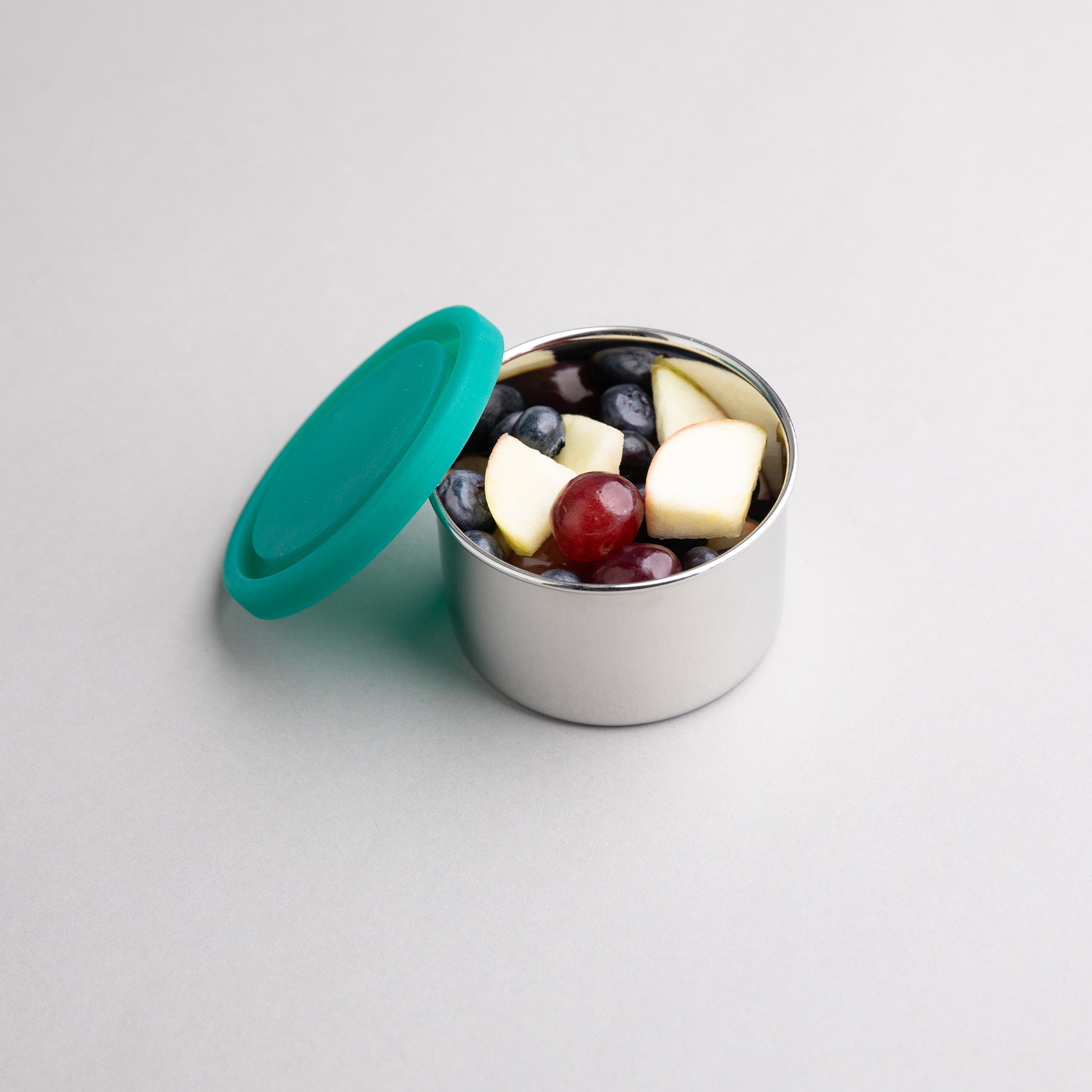 Stainless steel snack box filled with fruit with a green silicone lid