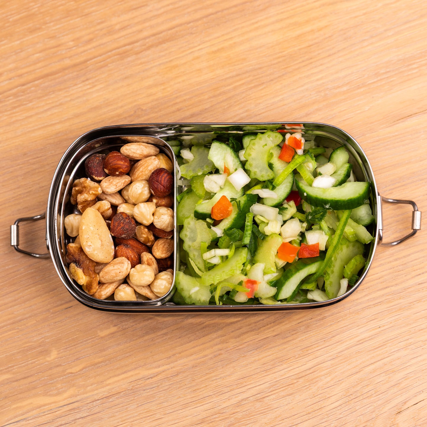 Stainless steel bento lunch box filled with nuts and salad on a school table