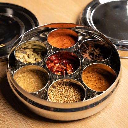 Stainless steel Masala dabba, spice box filled with spices on a wooden table