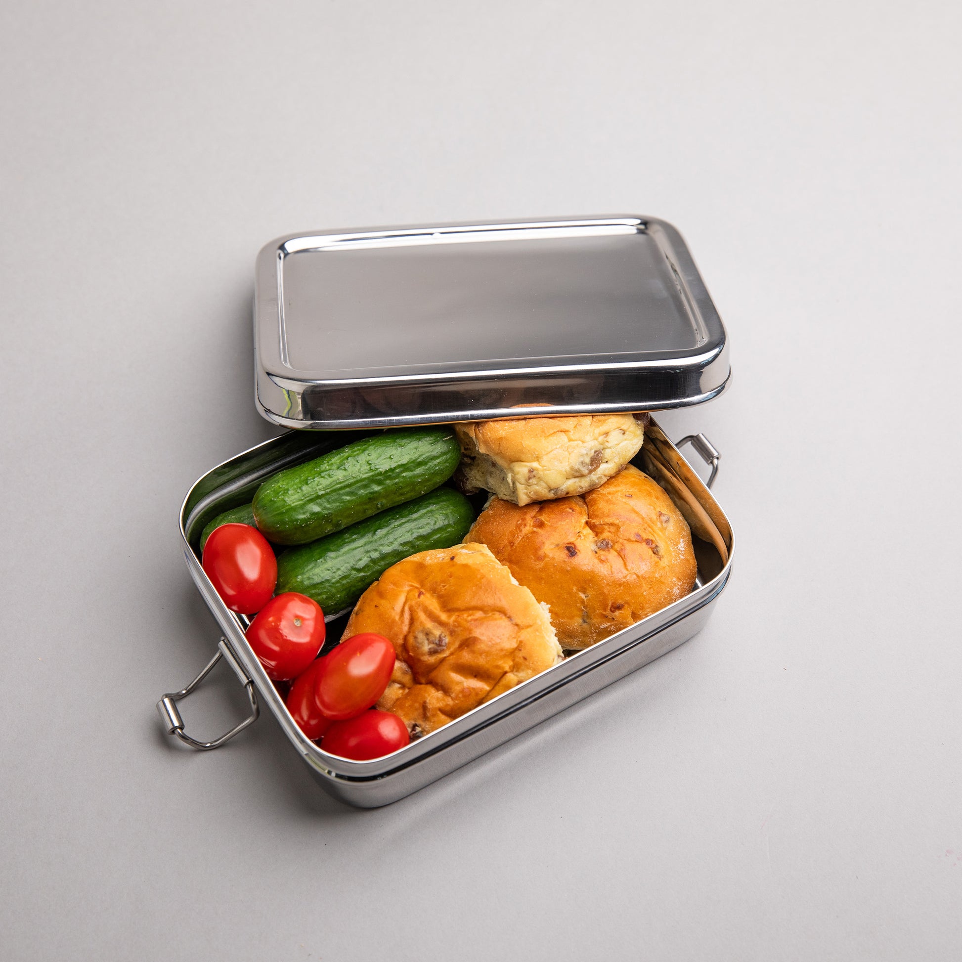 Stainless steel bread bin filled with cucumber tomatoes and bread. 