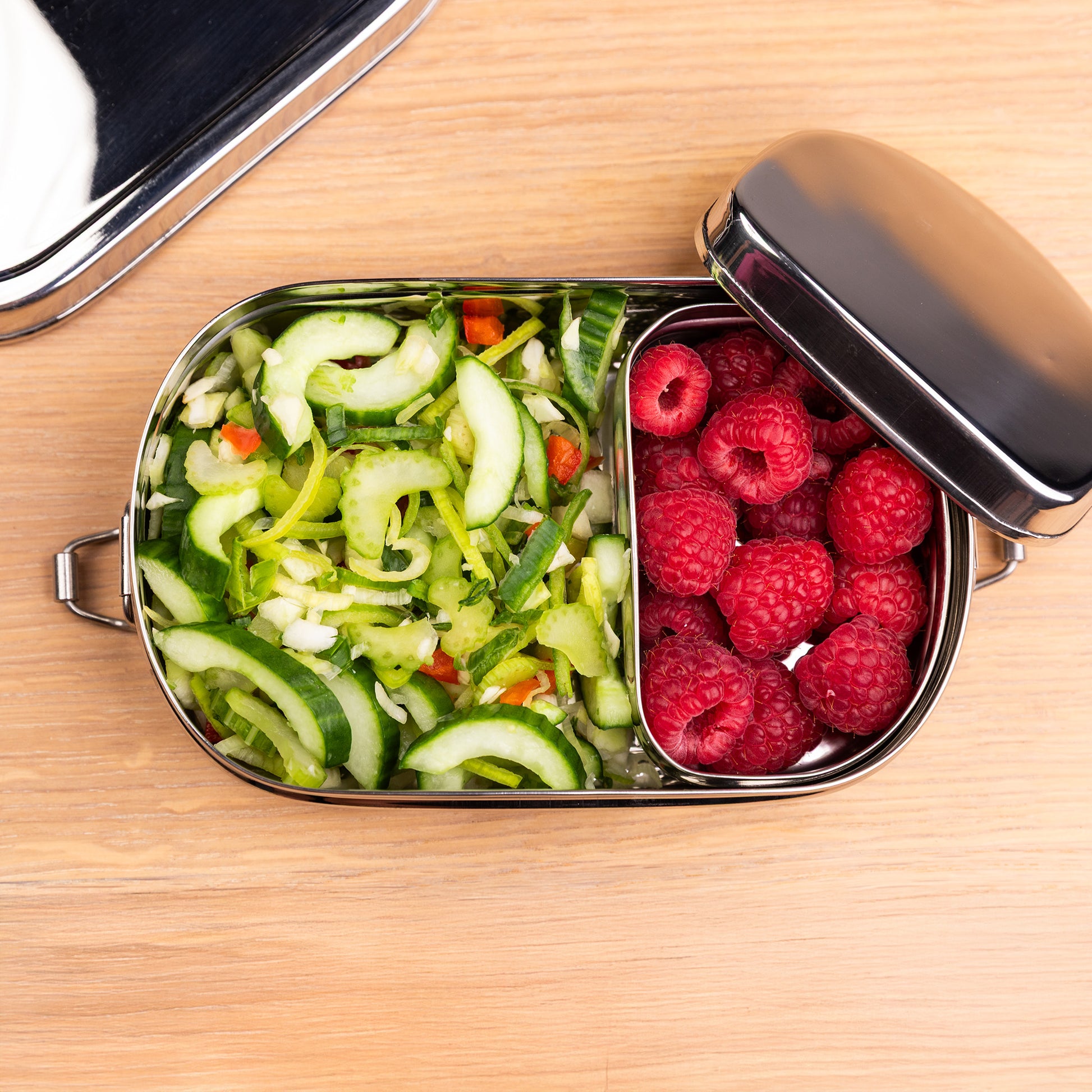 Stainless steel lunch box for children from above filled with salad and raspberry on a school table