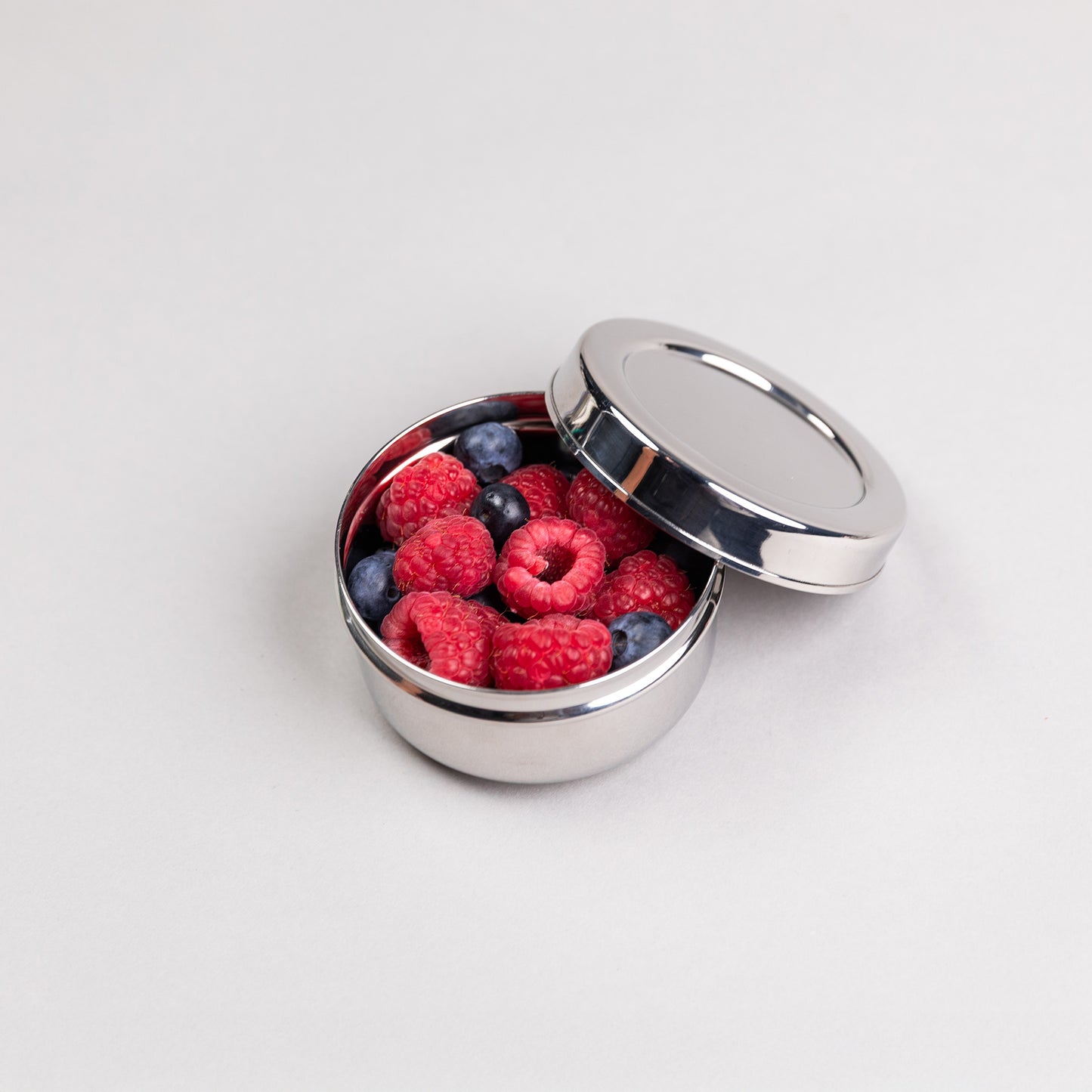 Medium stainless steel snack box round filled with raspberries.