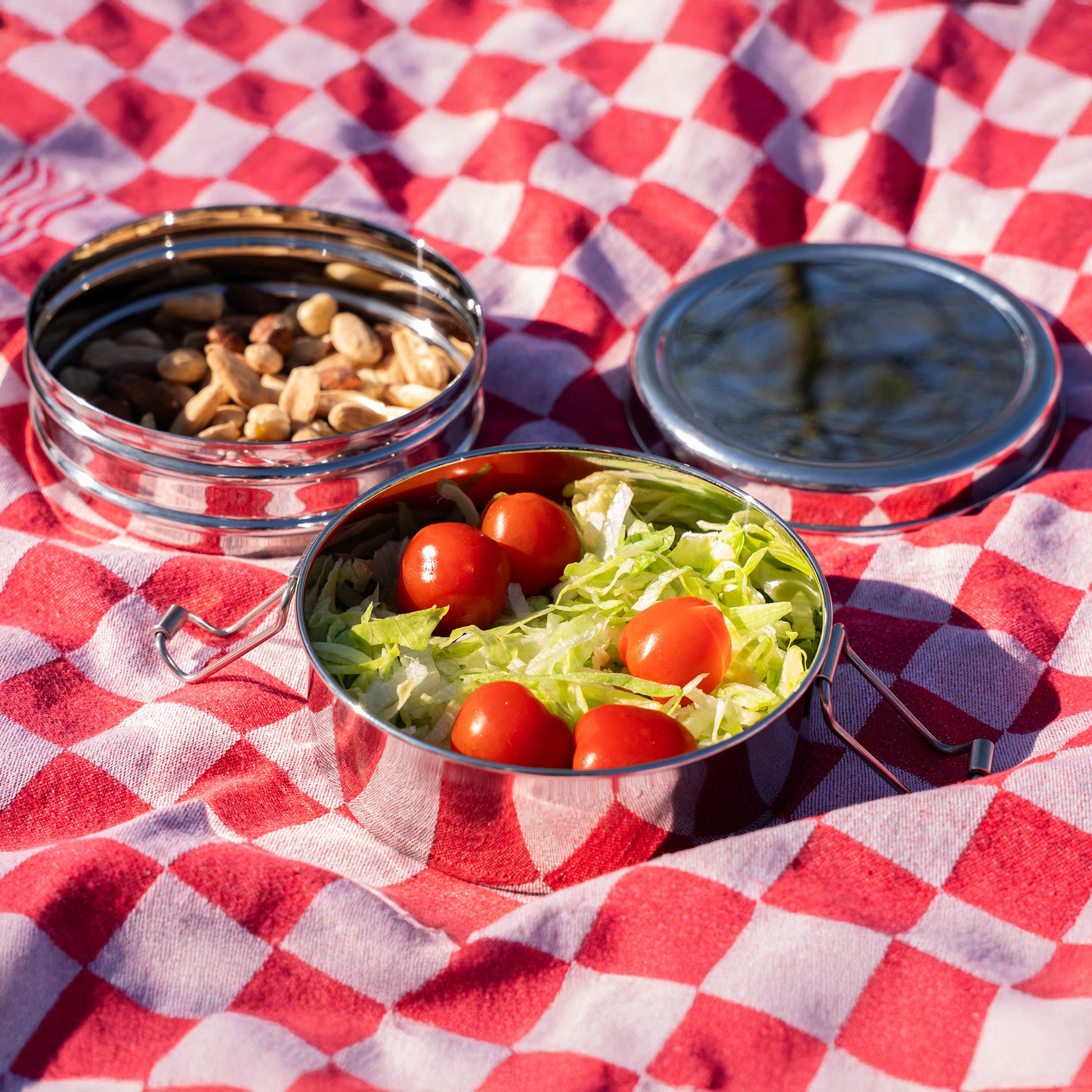 Opened stainless steel lunch box filled with nuts, lettuce and tomatoes