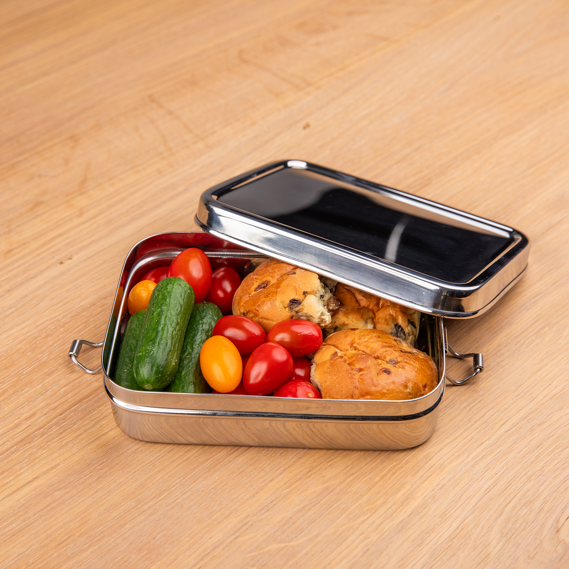 Stainless steel lunch box filled with bread and vegetables on a school table