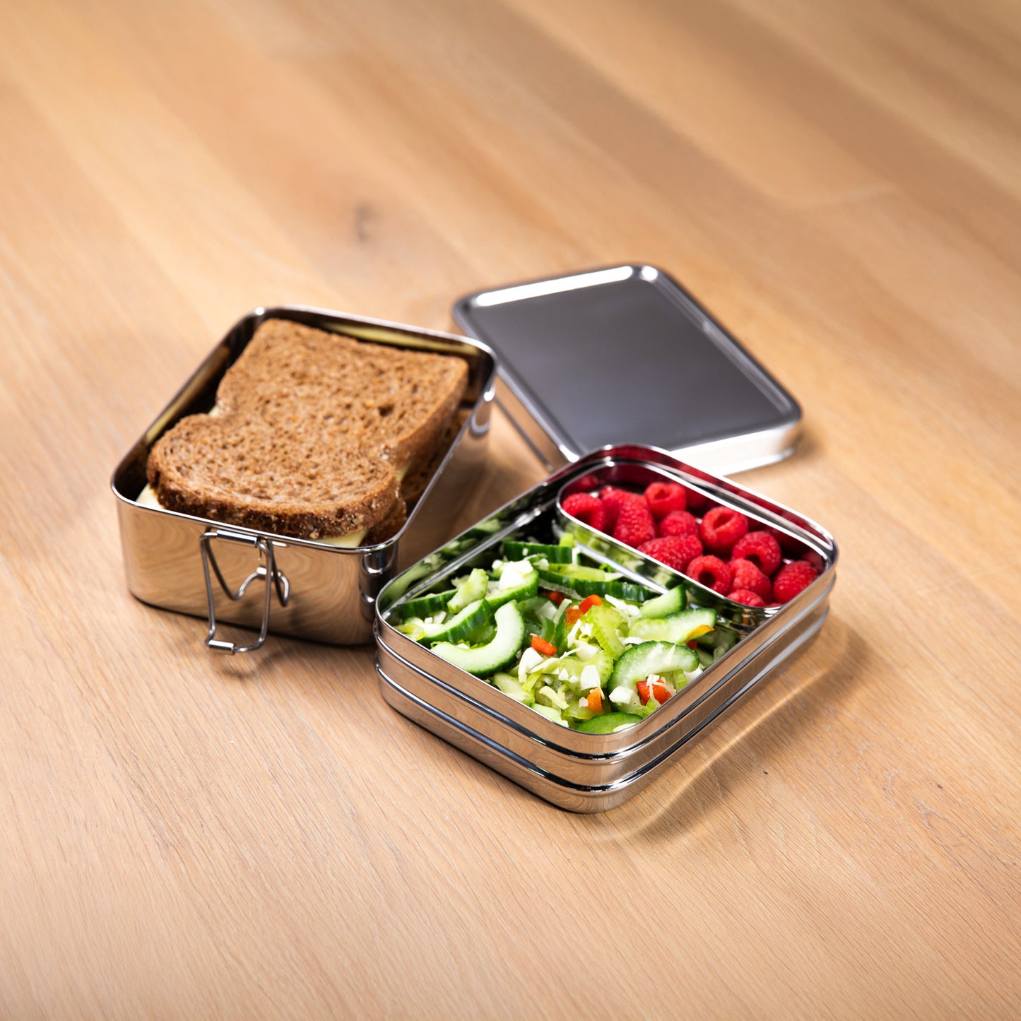 Stainless steel lunch box with fruit bowl on a wooden surface
