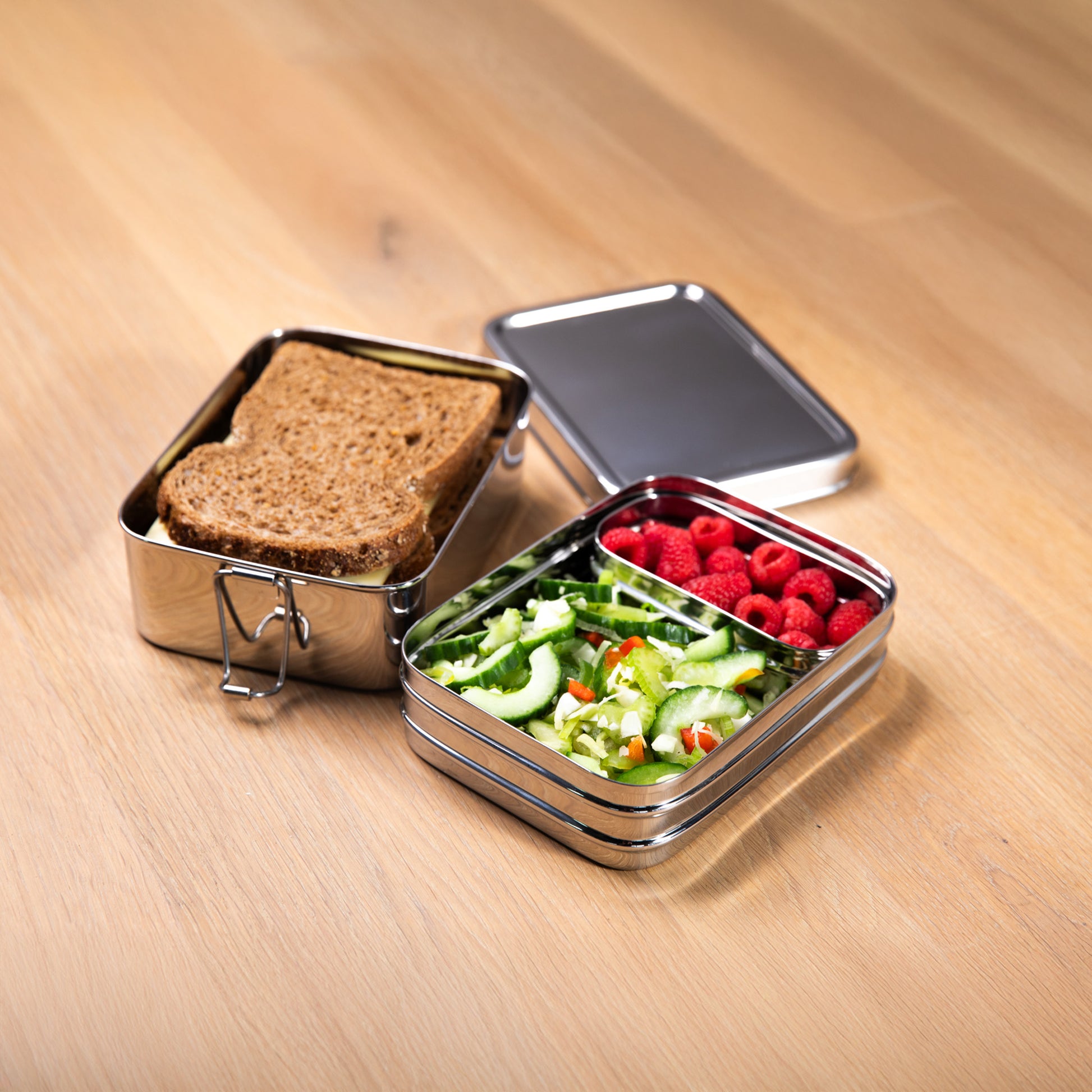 Stainless steel lunch box with fruit bowl on a wooden surface