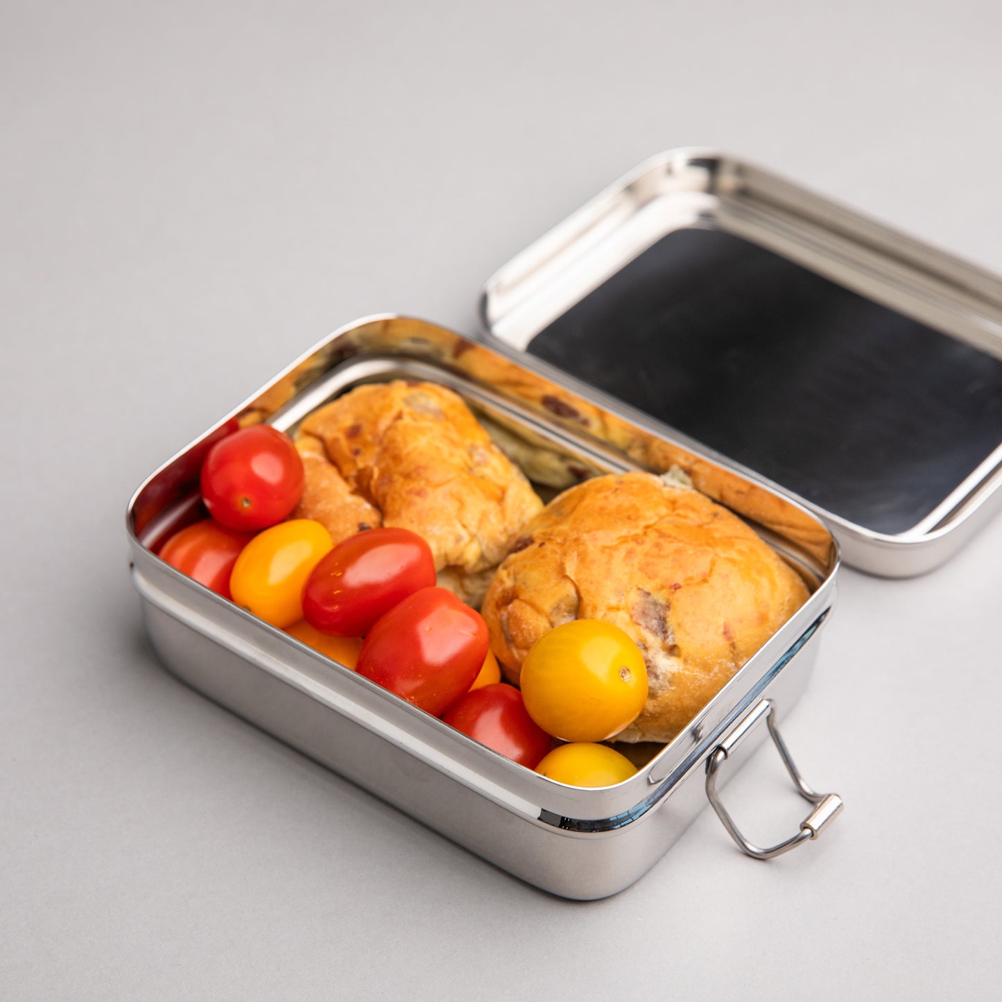 Stainless steel lunch box filled with mini currant buns and cherry tomatoes