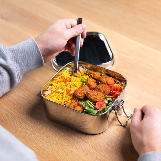 Stainless steel leak-proof lunch box filled with a meal of salads. A hand puts a fork in the lunch box