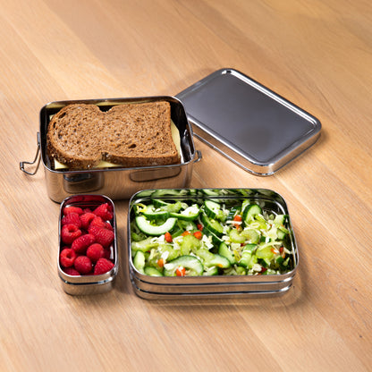 Stainless steel lunch box with a sandwich, lettuce and raspberries on a wooden table