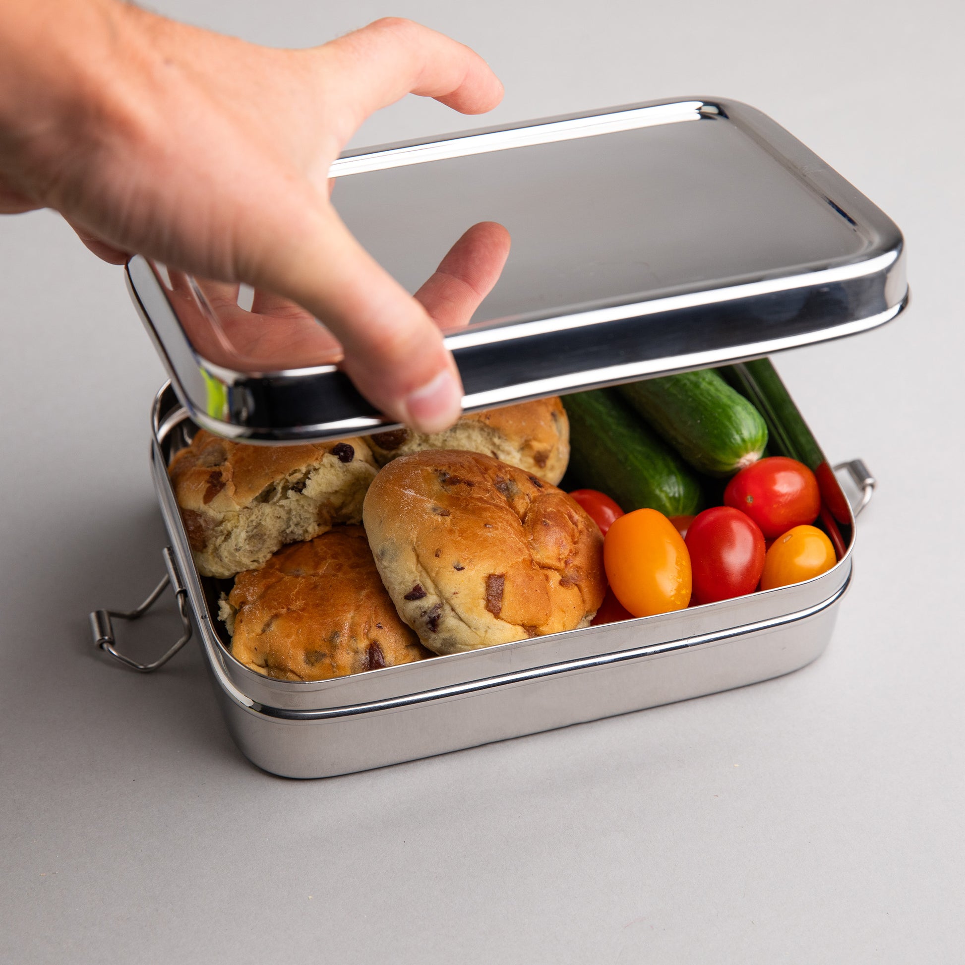 large stainless steel lunch box that is opened by a hand, filled with lunch