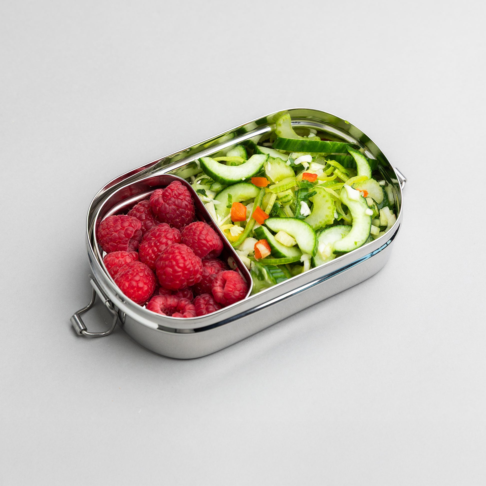 Stainless steel lunch box with compartments filled with raspberry and salad