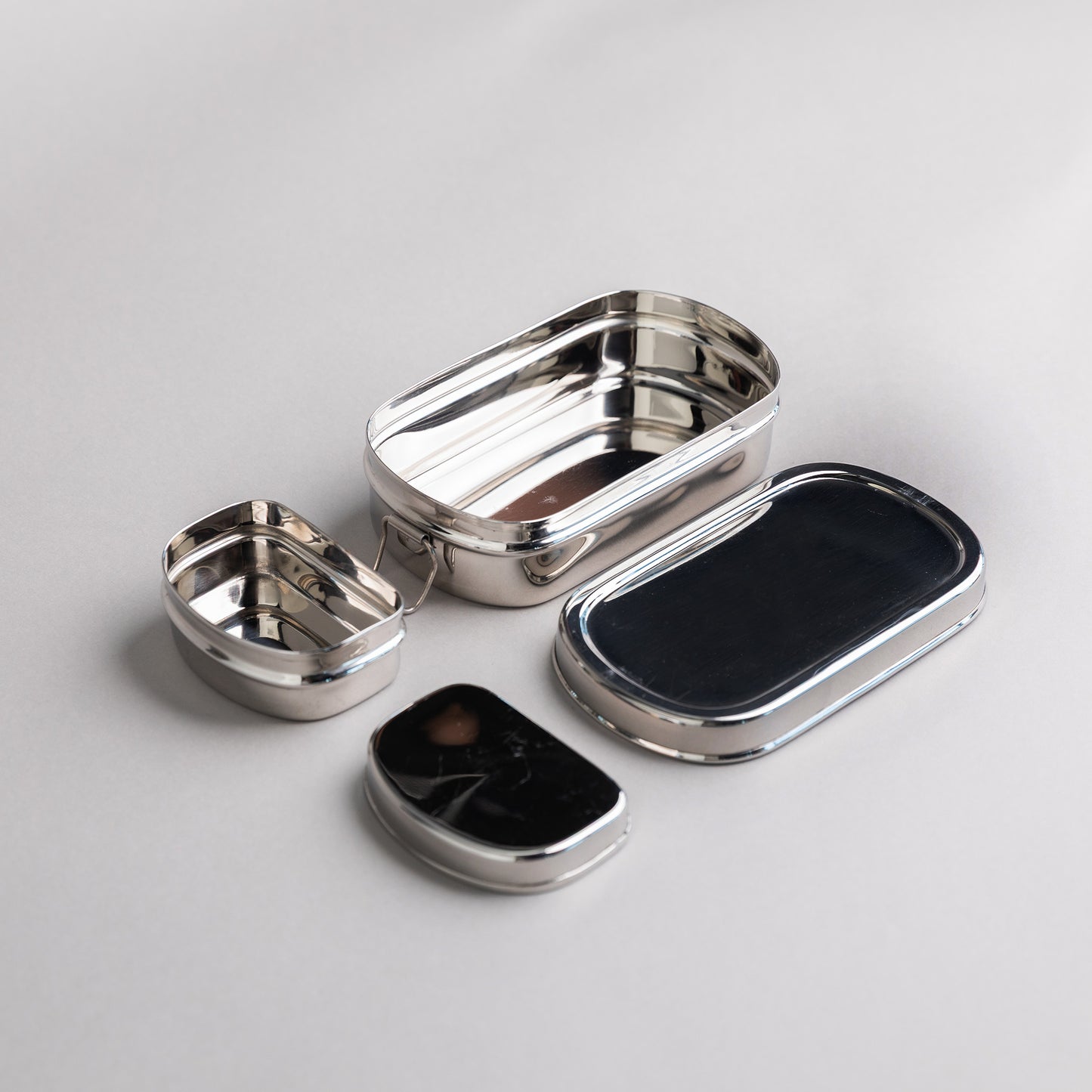 Stainless steel lunch box, snack box and two lids on a gray background