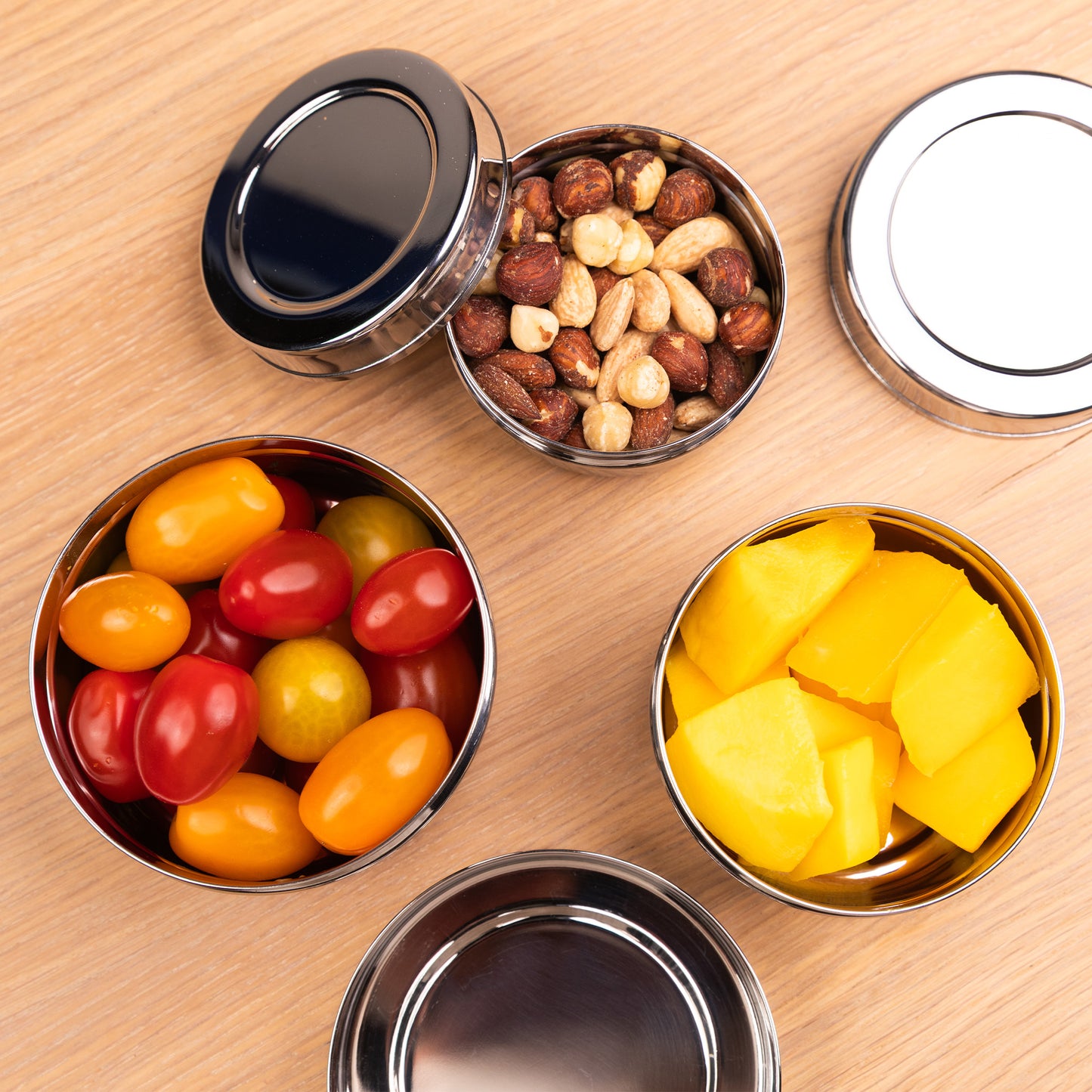 Stainless steel snack boxes filled with nuts, tomatoes and mango