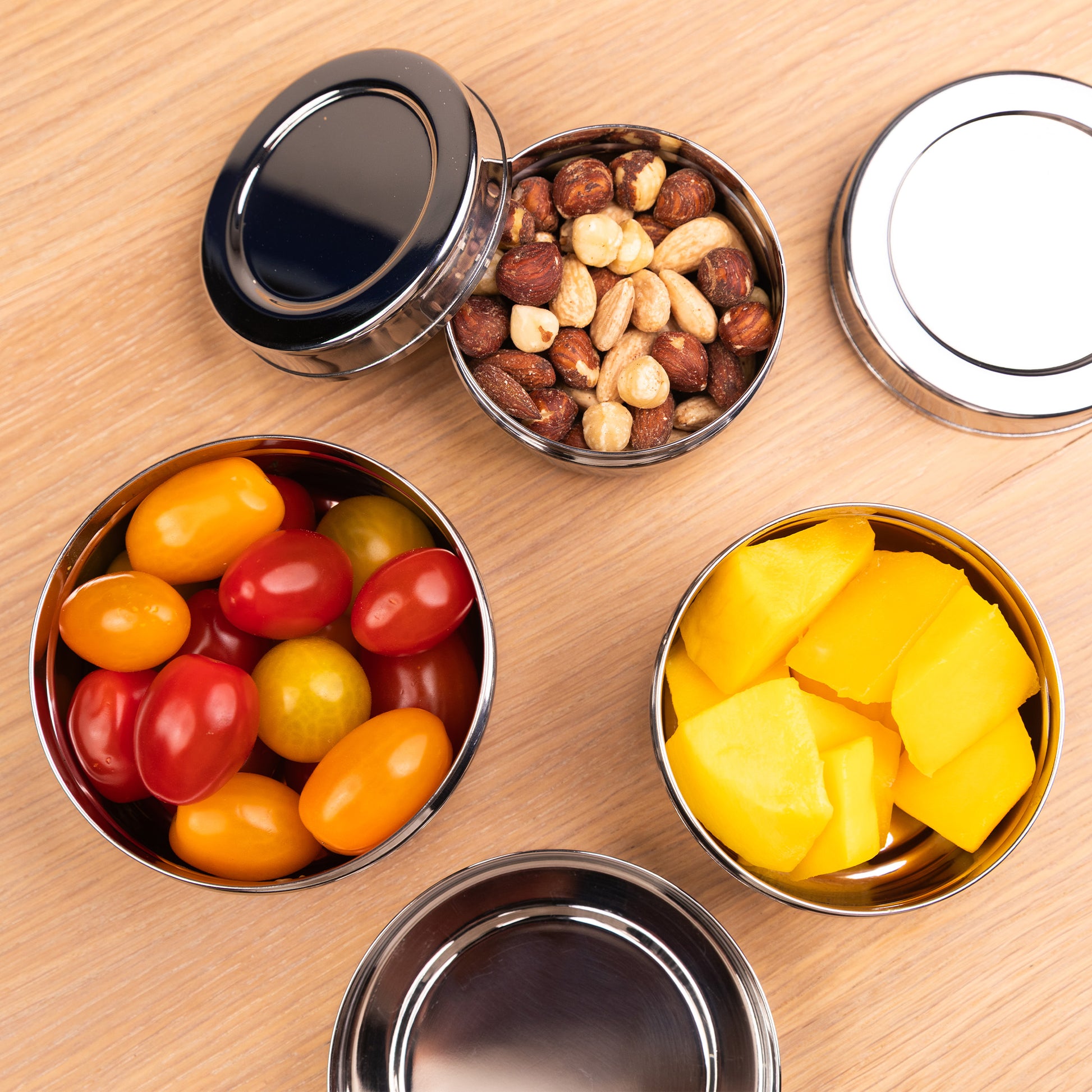 Stainless steel snack boxes filled with nuts, tomatoes and mango