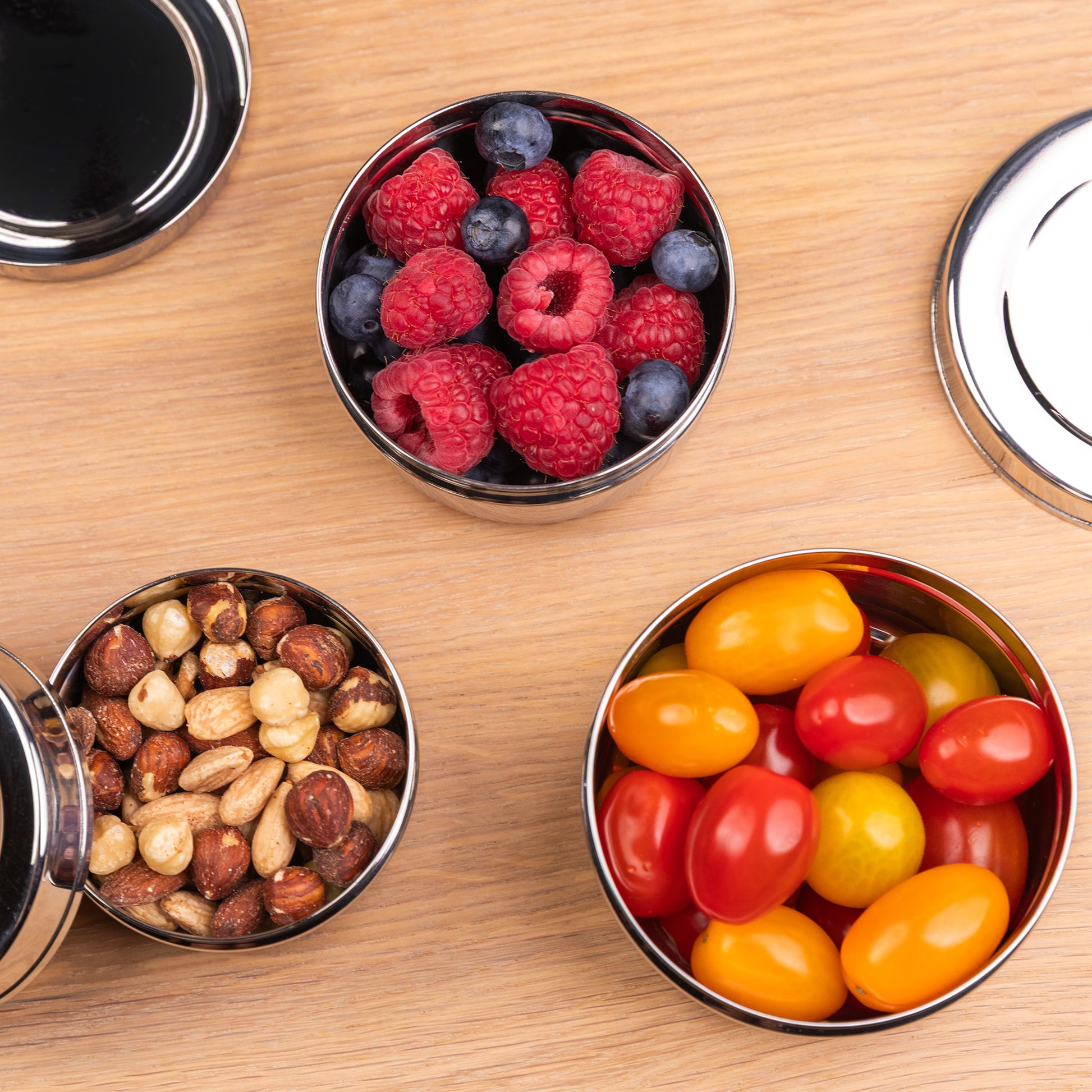 3 stainless steel snack boxes filled with fruit on a school table