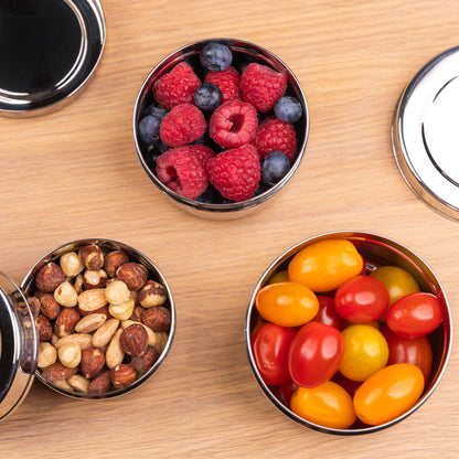 3 stainless steel snack boxes filled with fruit on a school table