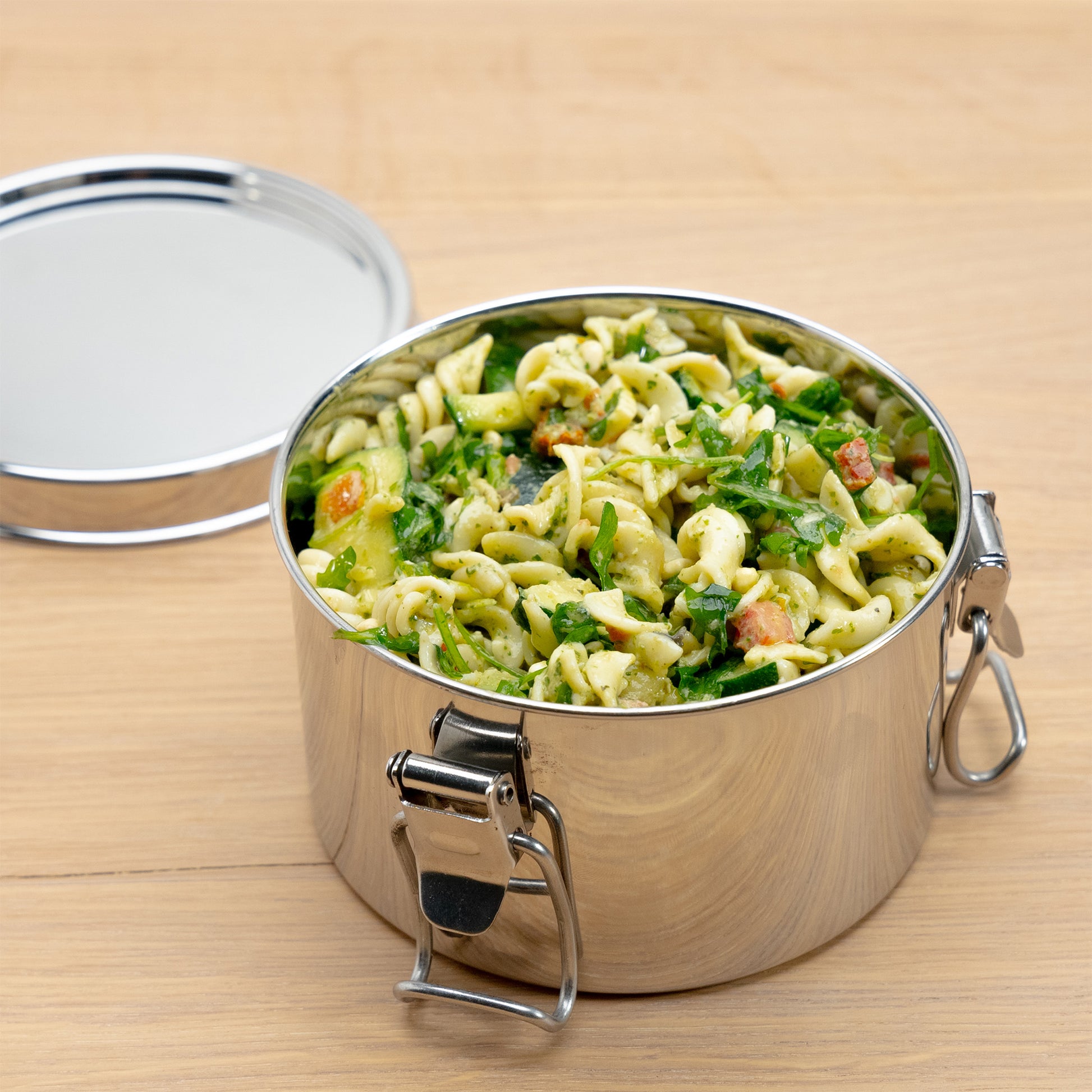 Stainless steel lunch box filled with pasta on a wooden table