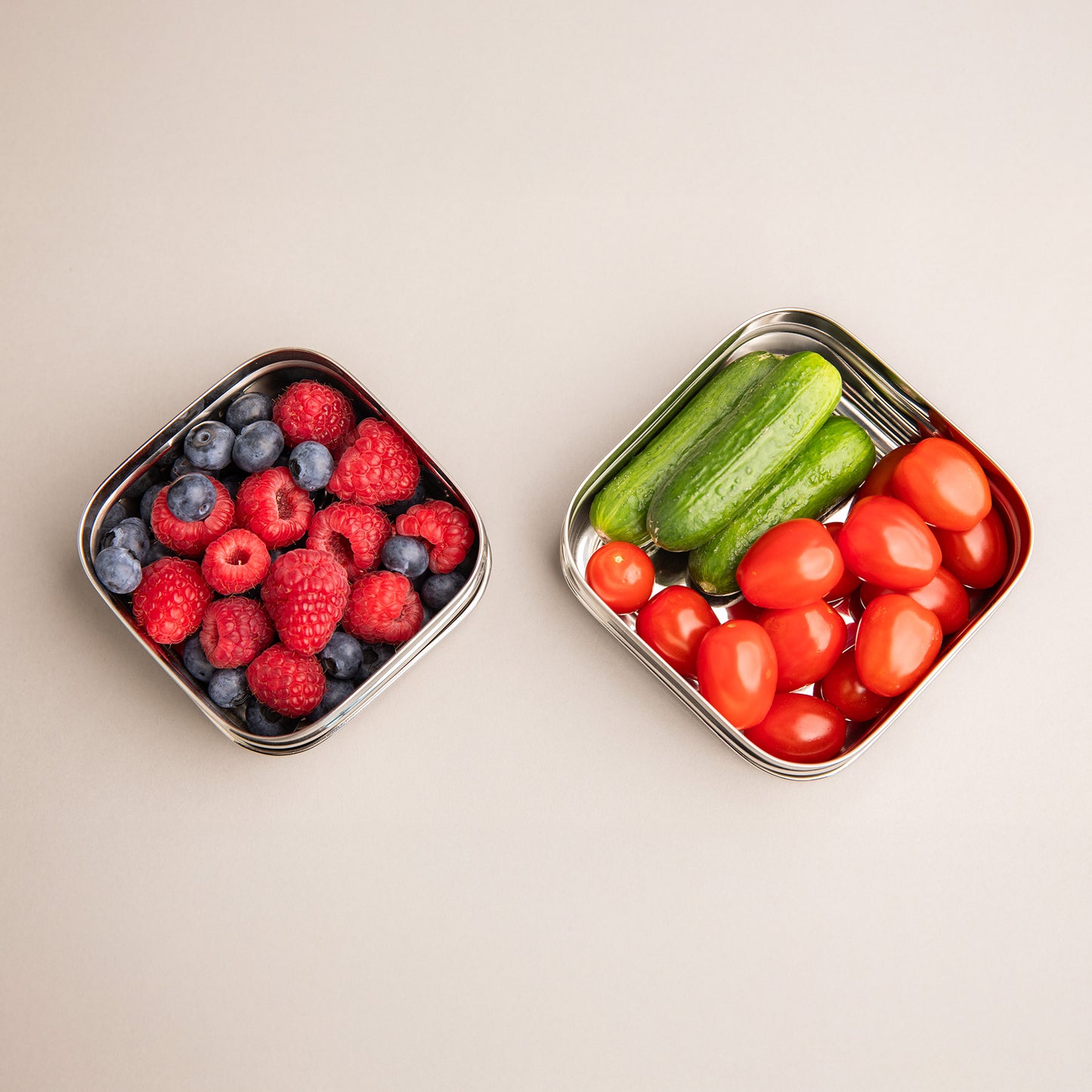 two stainless steel snack boxes filled with fruit and vegetables