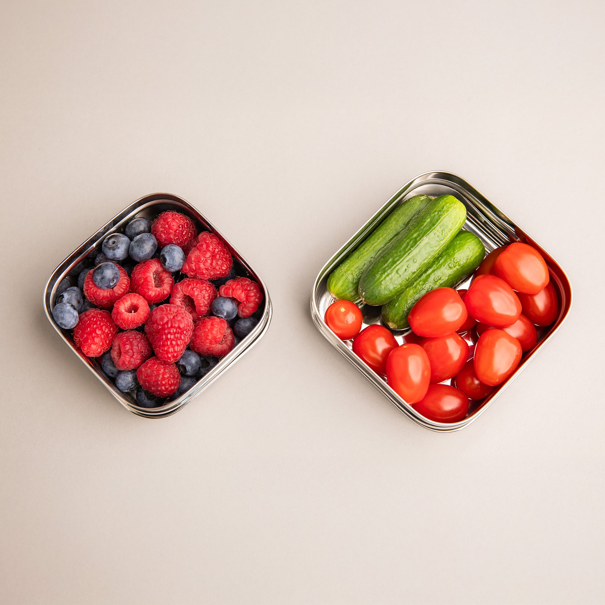 two stainless steel snack boxes filled with fruit and vegetables