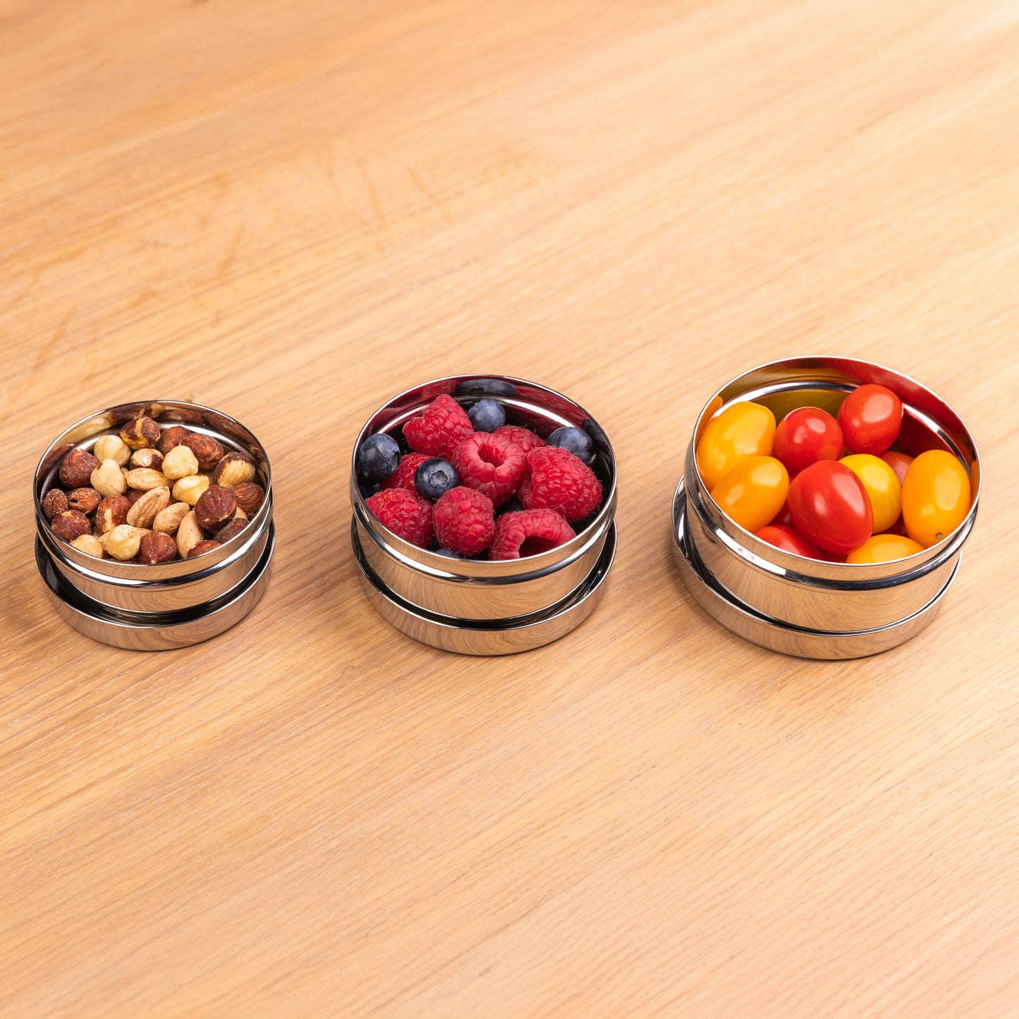 3 stainless steel snack boxes in a row filled with fruit and vegetables