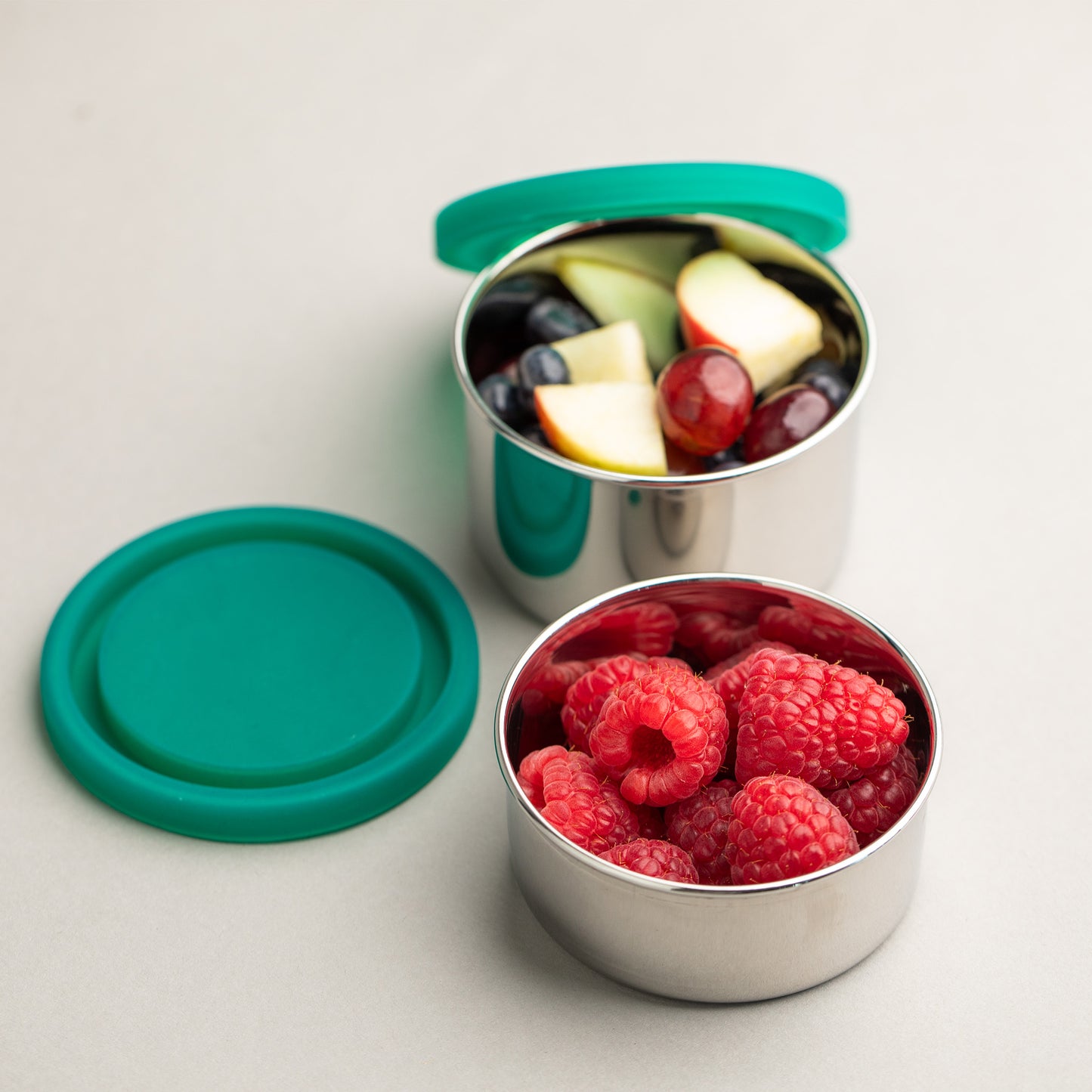 two stainless steel snack boxes filled with fruit.