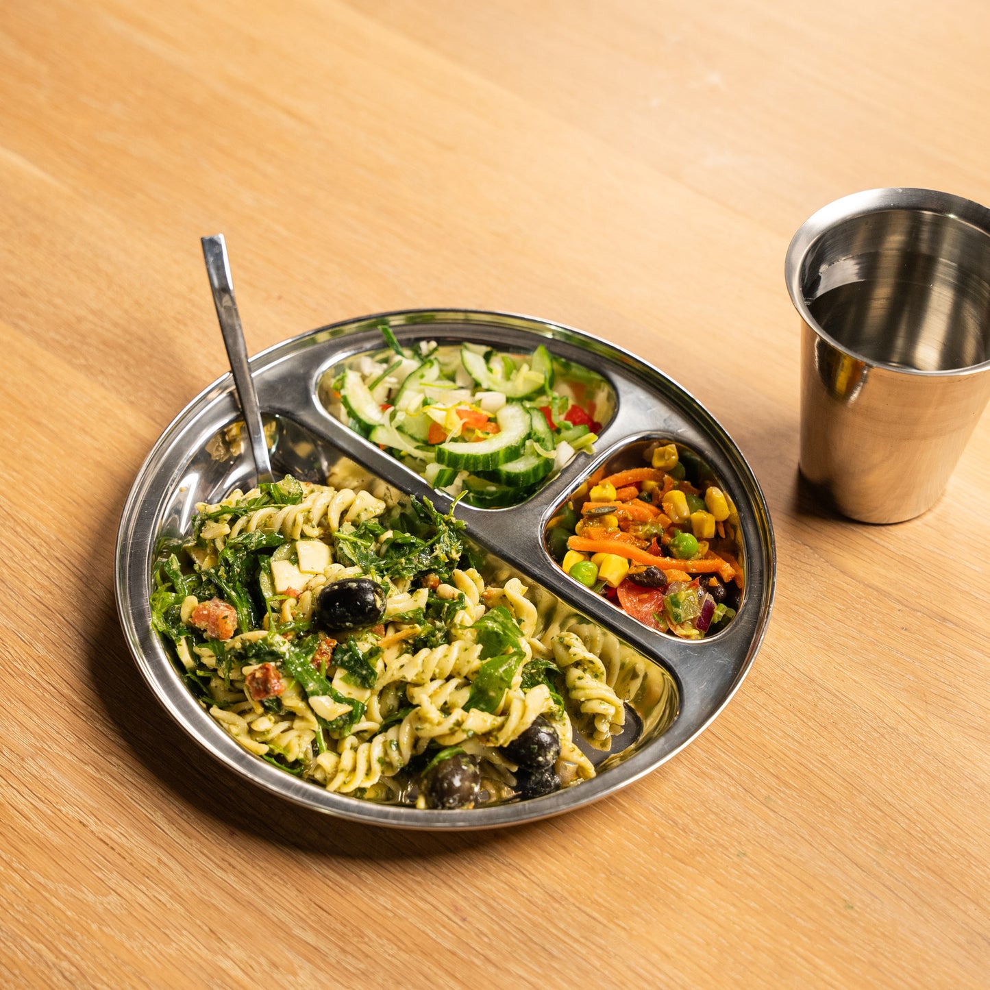 Stainless steel plate with compartments from India on a table with spoon and a glass