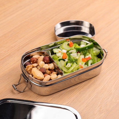 Stainless steel lunch box for children filled with nuts and a salad on a school table