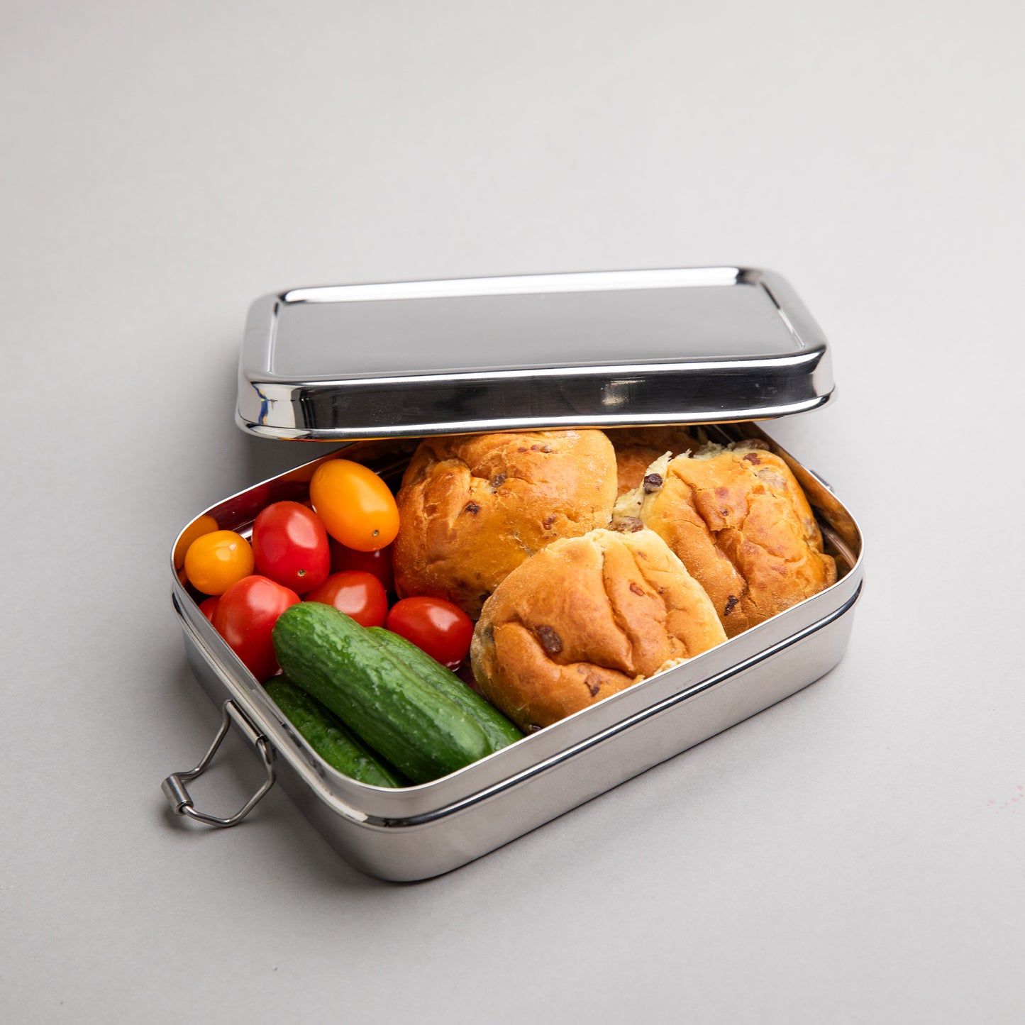 Stainless steel lunch box opened and filled with currant buns and tomatoes