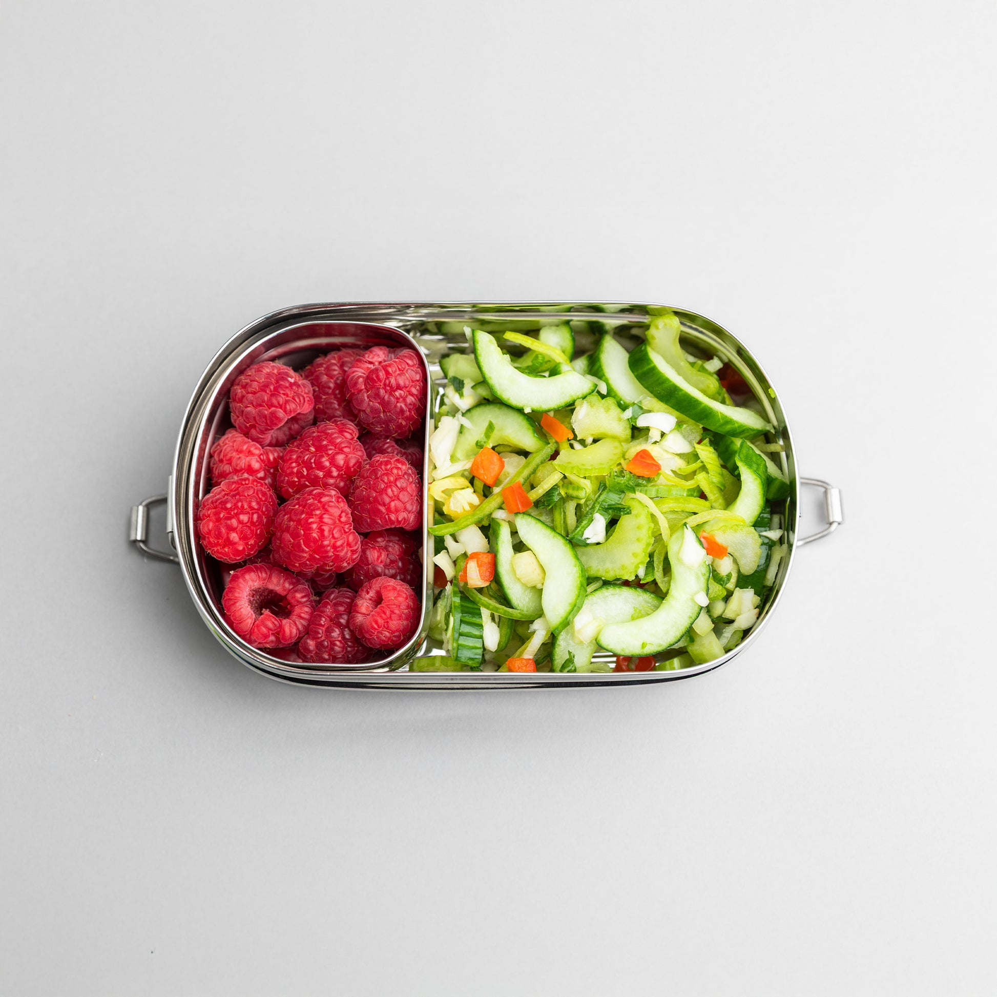lunch box with compartments on top. filled with raspberry and salad