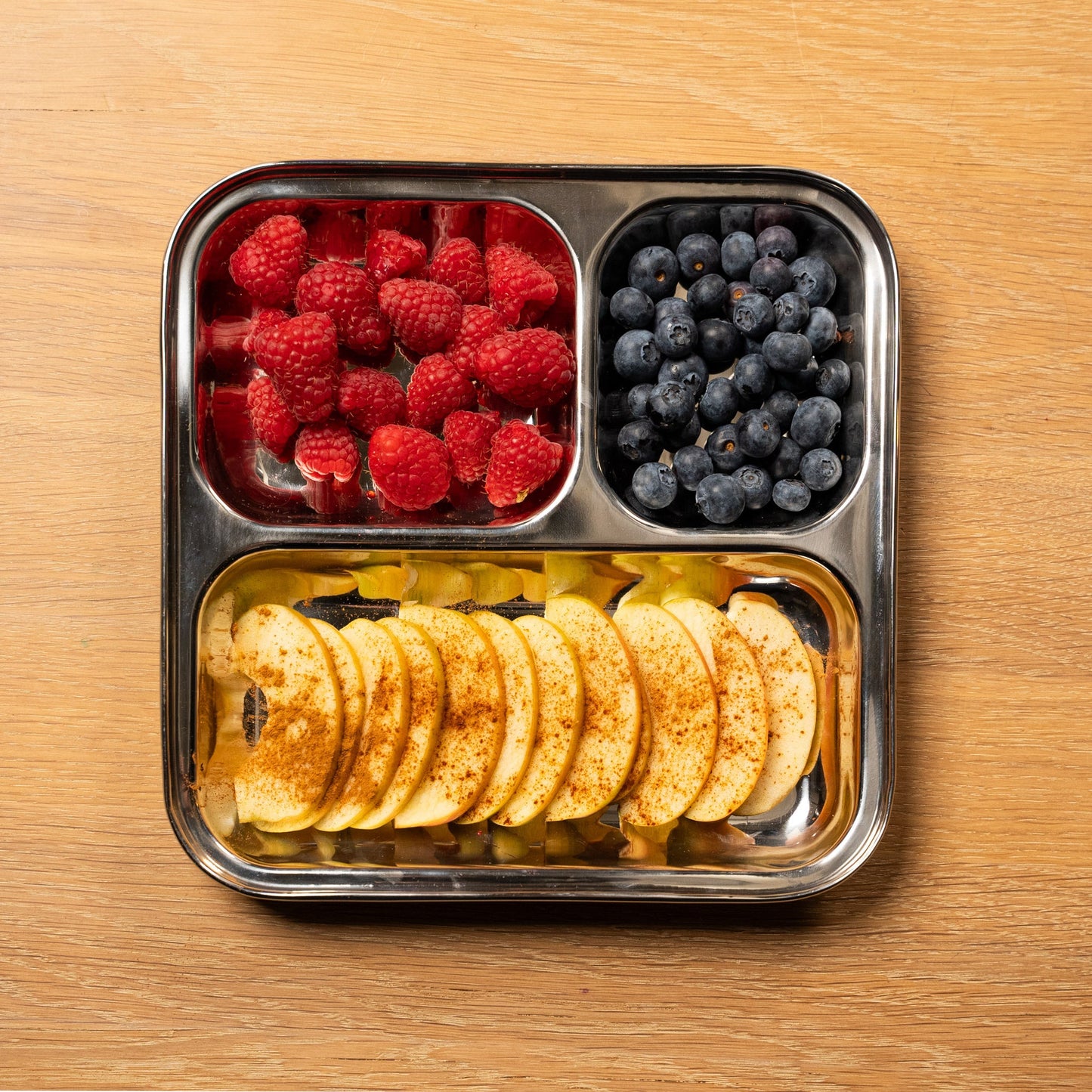 top view stainless steel children's plate with compartments. filled with apple and raspberry